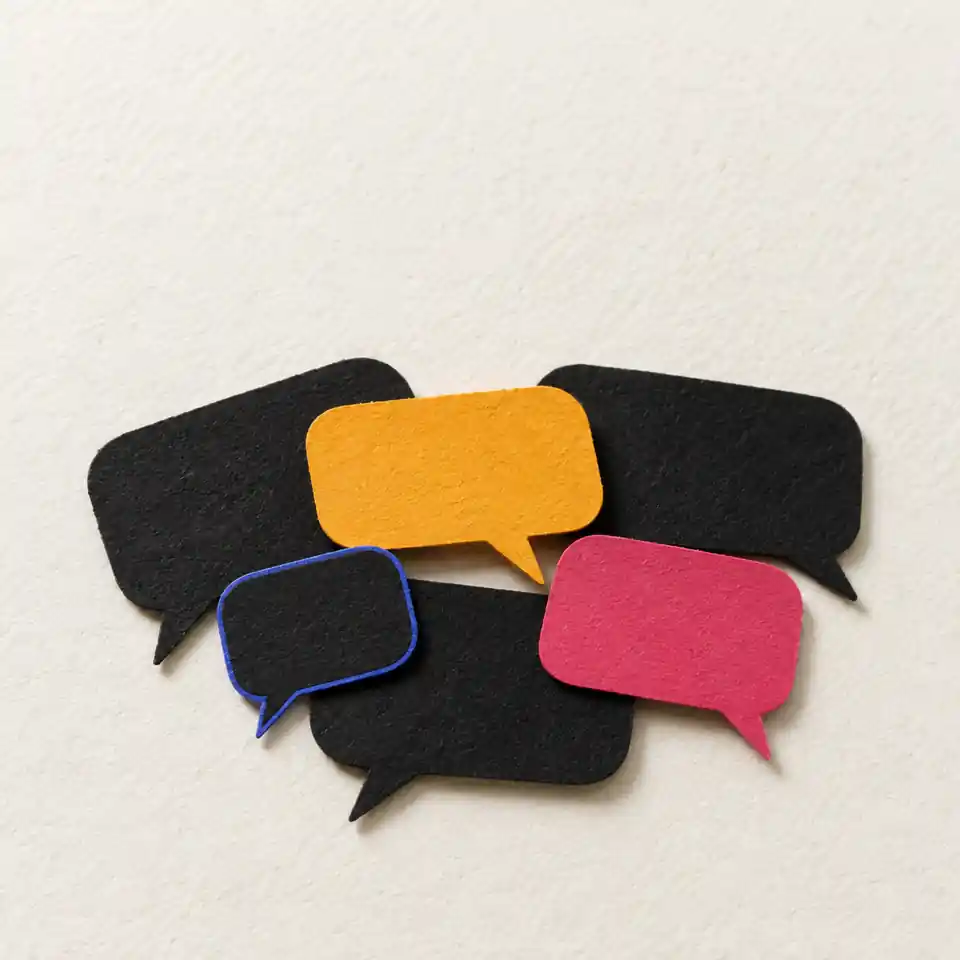 A loose stack of paper speech-bubble cut-outs in ink, saffron, rose and blue on a paper-white surface.